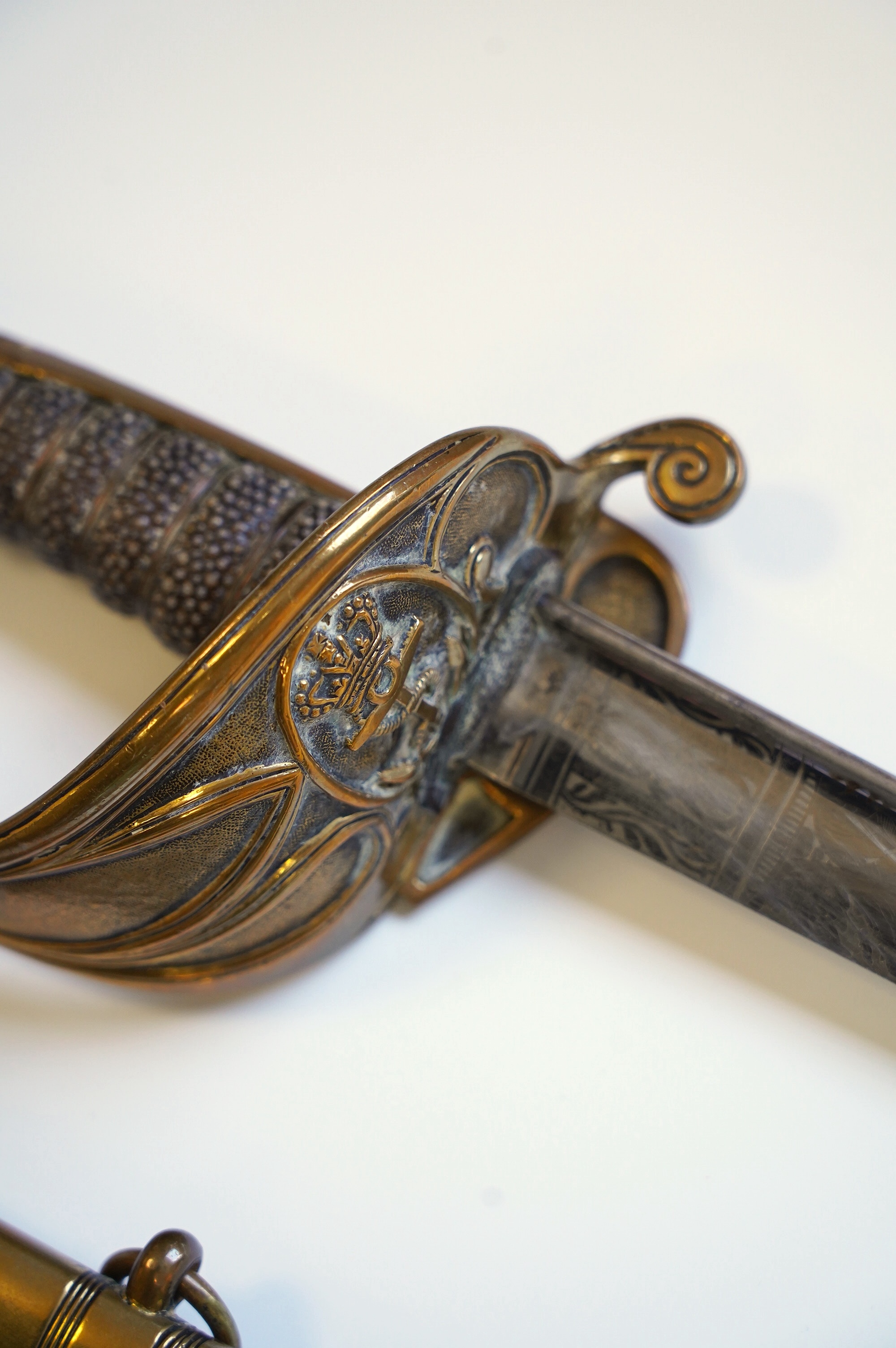 An early 19th century Royal Navy officer's sword with engraved blade, folding knuckle guard, lion’s head pommel and shagreen grip, leather scabbard with brass fittings, blade 73.5cm. Condition - fair, some wear overall.